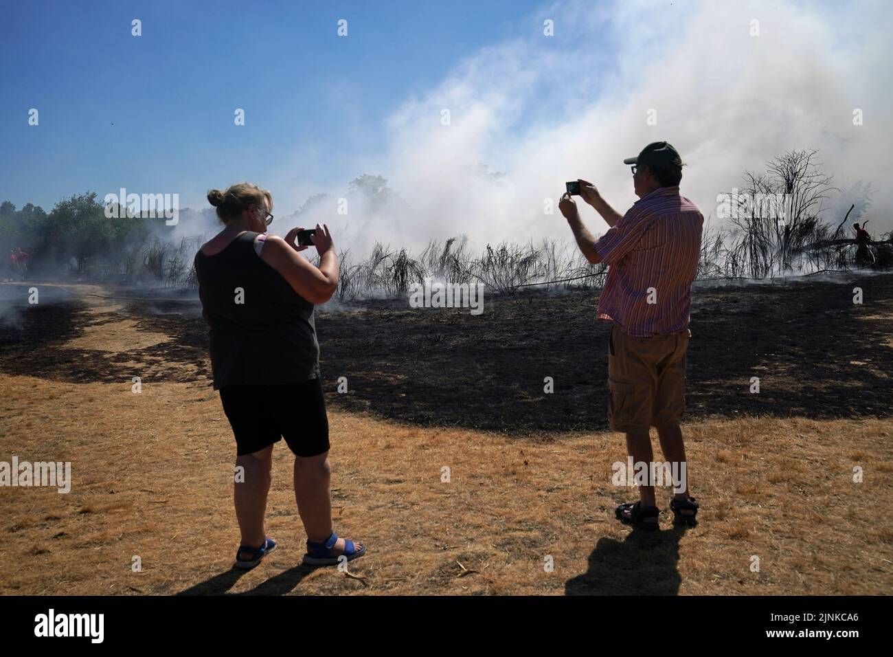 Passers by take photos of firefighters battling a grass fire on Leyton flats in east London, as a drought has been declared for parts of England following the driest summer for 50 years. Picture date: Friday August 12, 2022. Stock Photo
