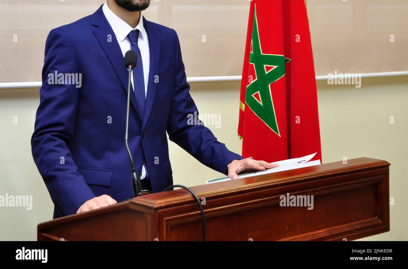 A Moroccan young man in a formal suit giving a lecture in front of the Moroccan flag Stock Photo