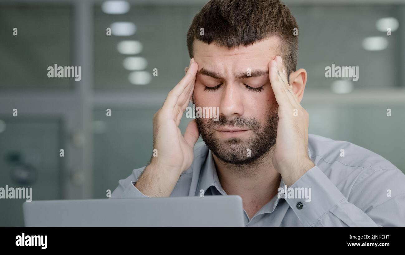 Close-up tired pensive businessman looking at laptop screen suffering from overwork feeling headache painful symptom migraine rubbing temples young Stock Photo