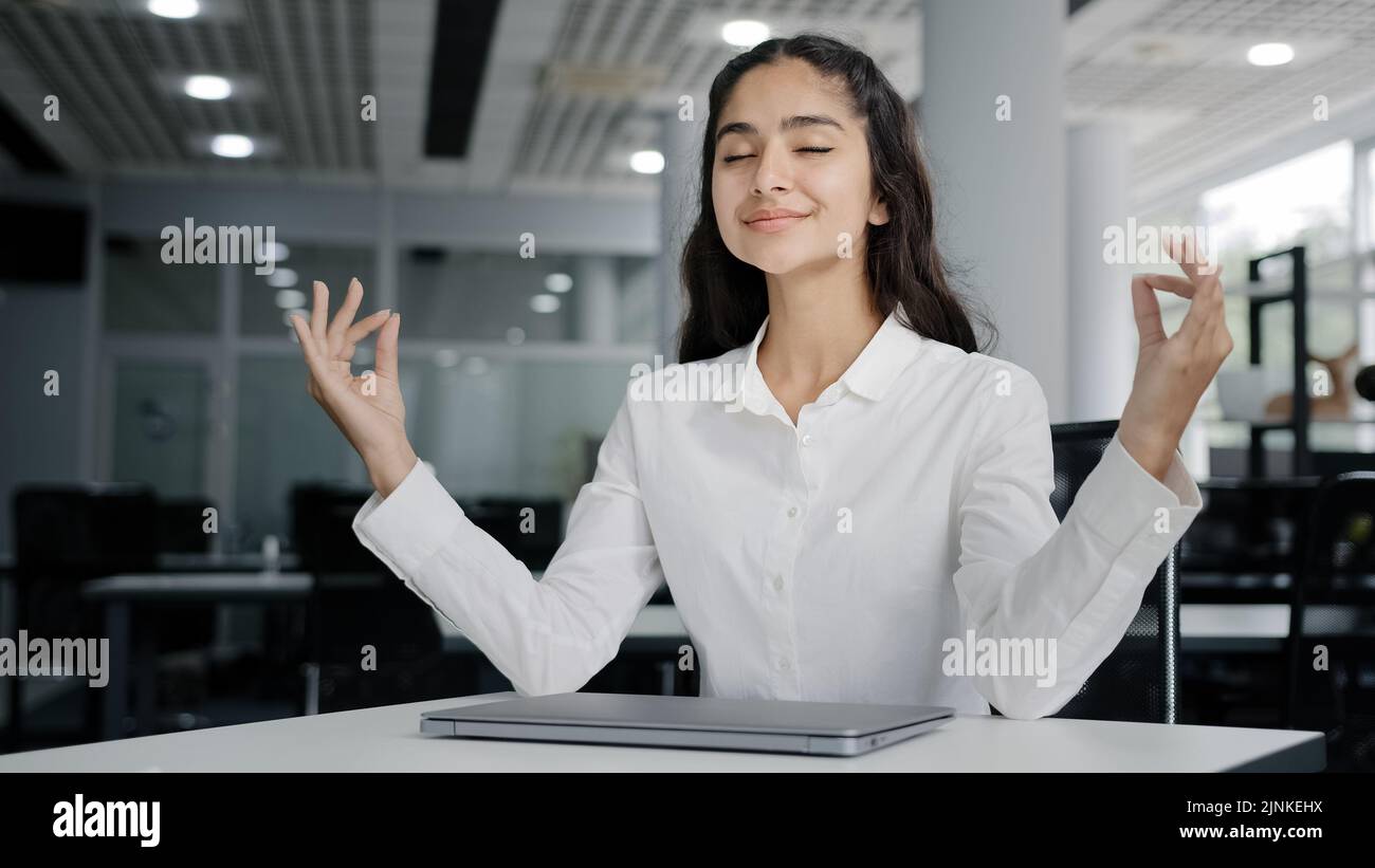 Young tired woman office worker working on laptop typing report finishes work calm balanced female manager meditates with closed eyes resting at Stock Photo
