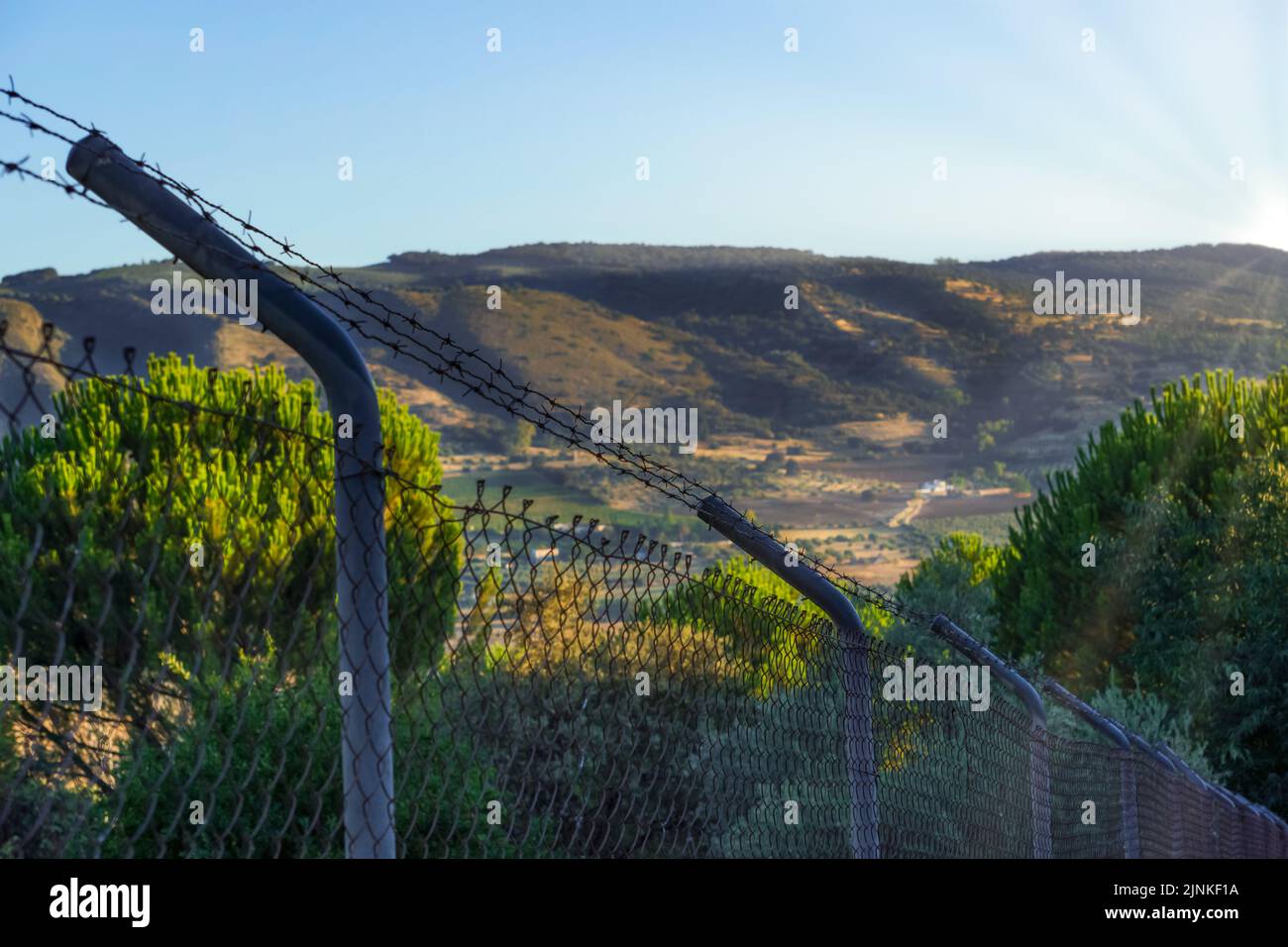 view of a barbed wire fence with a mountain landscape at dawn in the background Stock Photo