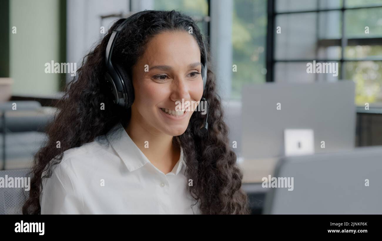 Young positive woman in headphones communicates via video call call center operator talks to customer on online conference via webcam on computer Stock Photo