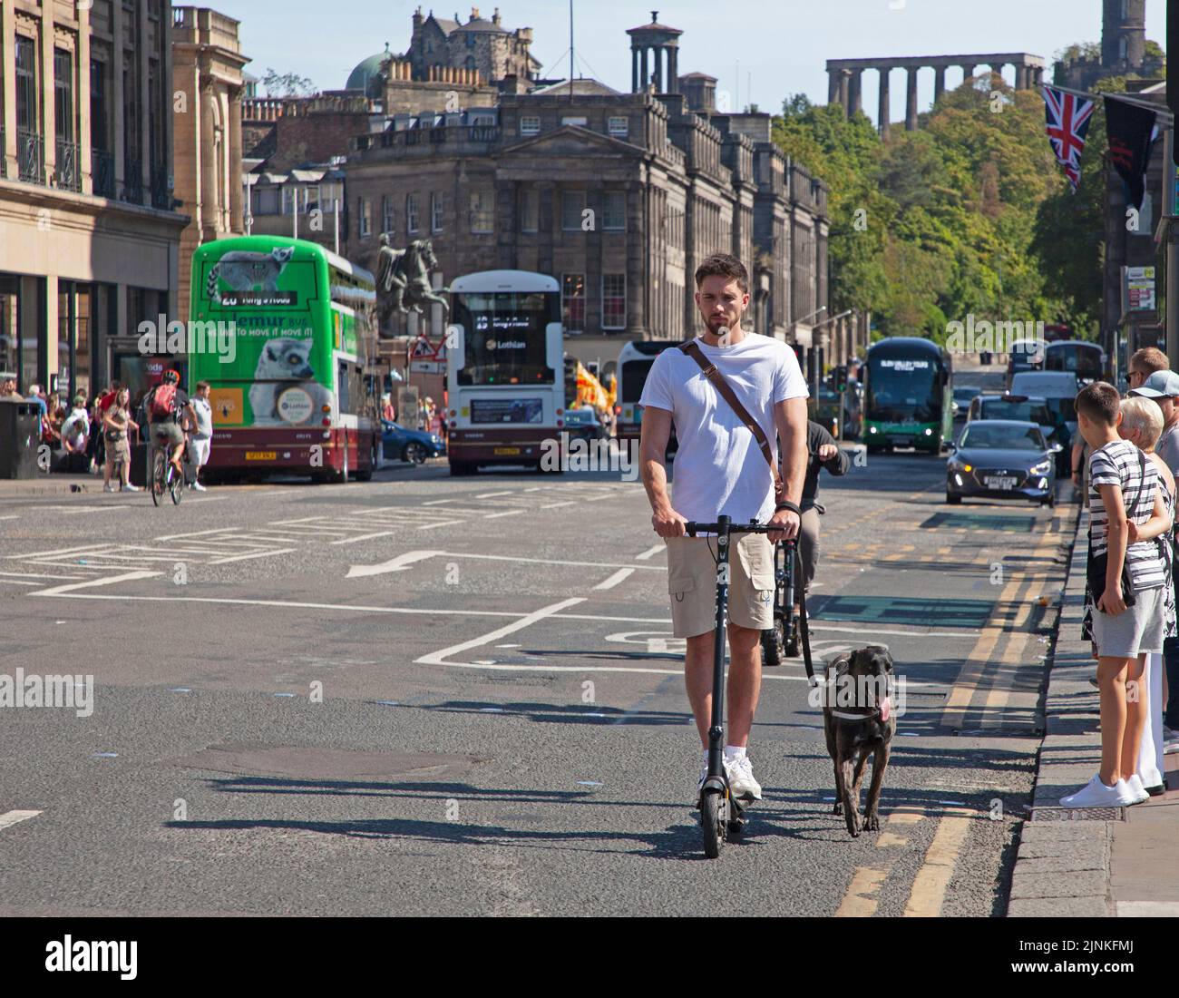 Edinburgh city centre, Scotland, UK. 12th August 2022. Edinburgh busy for the 8th day of Edinburgh Festival Fringe at various venues in the capital city for the end of the first full week. Temperature 21 degrees centigrade for those out and about. Pictured: Novel way to take a dog for a walk using an electric scooter on the road in Princes Street. Credit: Scottishcreative/alamy live news. Stock Photo