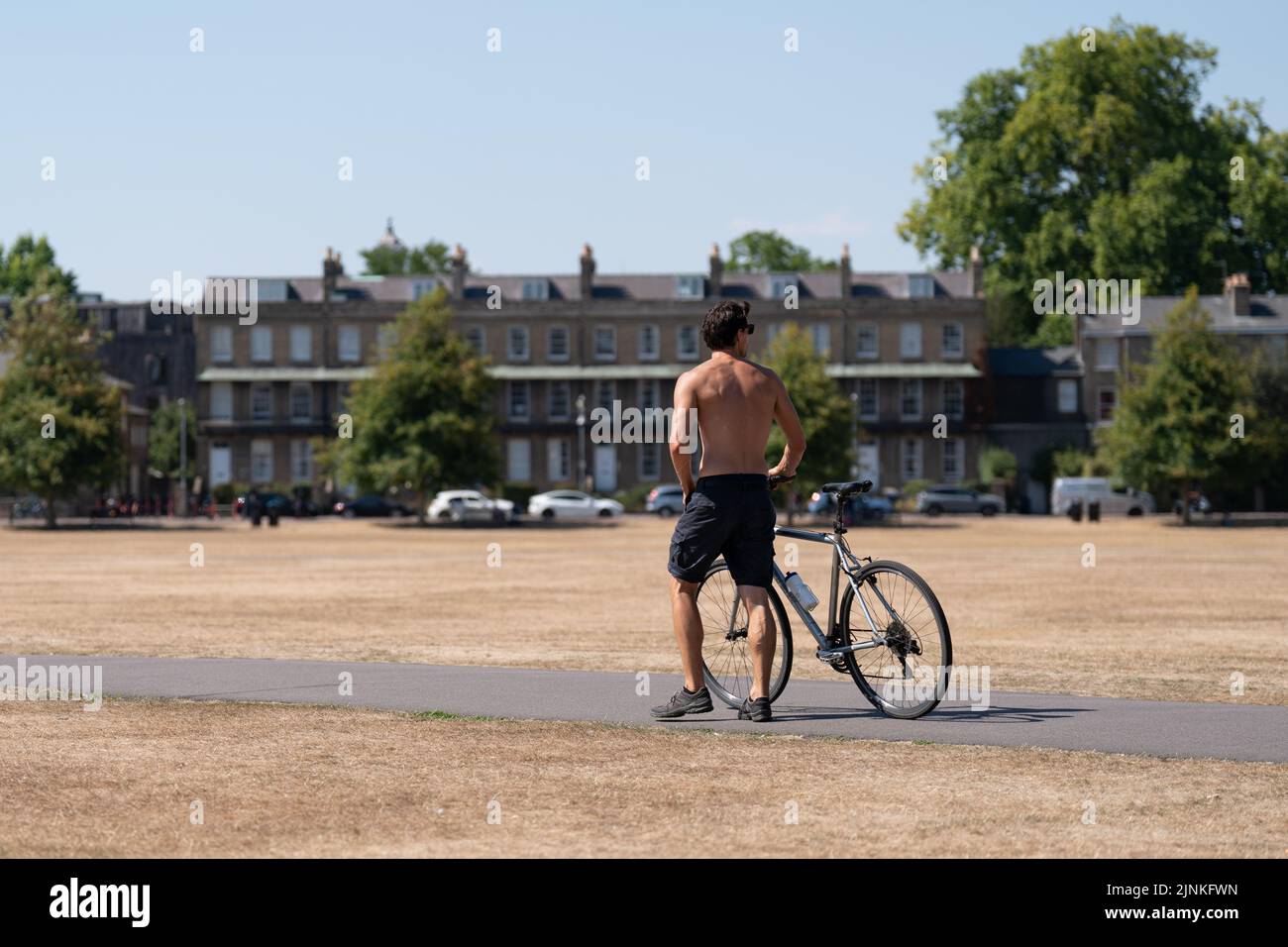 A man pushes his bike across Parker's Piece in Cambridge, as a drought has been declared for parts of England following the driest summer for 50 years. Picture date: Friday August 12, 2022. Stock Photo