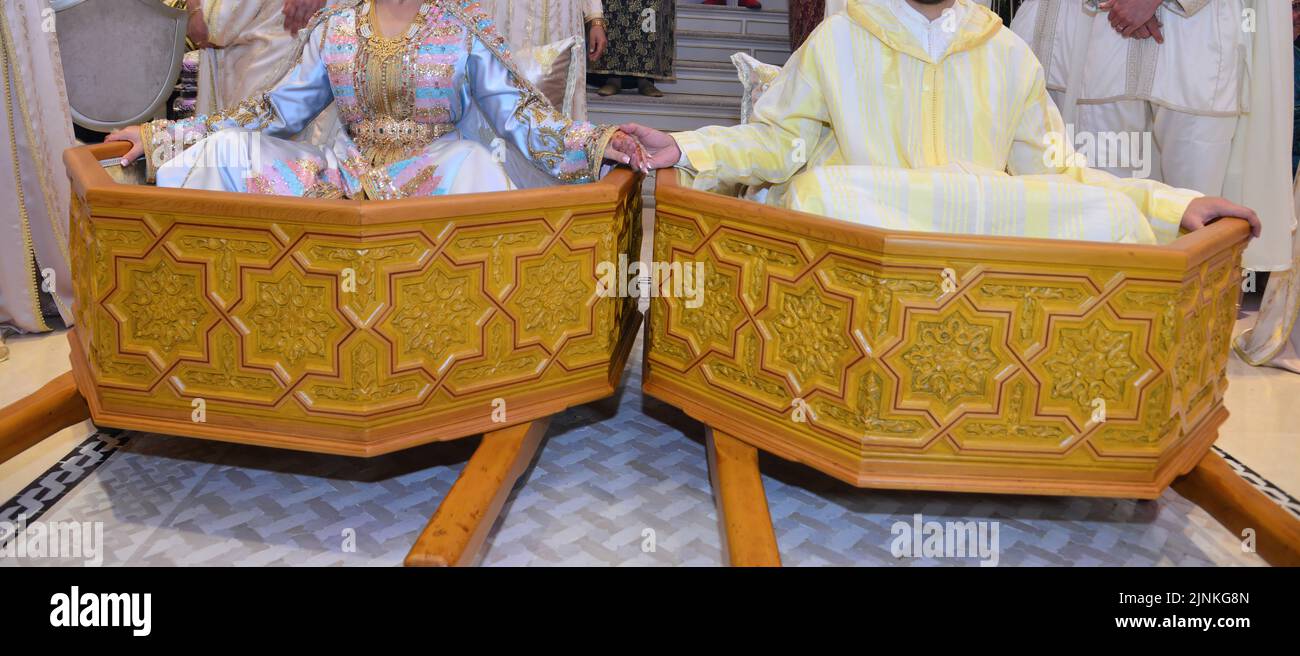 Moroccan groom and bride sitting on top of a wooden box used to celebrate the Moroccan wedding Stock Photo