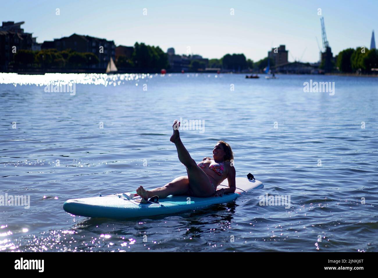 A woman lies on a paddleboard in the Isle of Dogs, in east London. A drought is set to be declared for some parts of England on Friday, with temperatures to hit 35C making the country hotter than parts of the Caribbean. Picture date: Friday August 12, 2022. Stock Photo