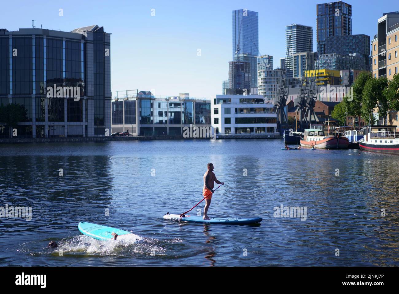 A man stands on a paddleboard in the Isle of Dogs, in east London. A drought is set to be declared for some parts of England on Friday, with temperatures to hit 35C making the country hotter than parts of the Caribbean. Picture date: Friday August 12, 2022. Stock Photo