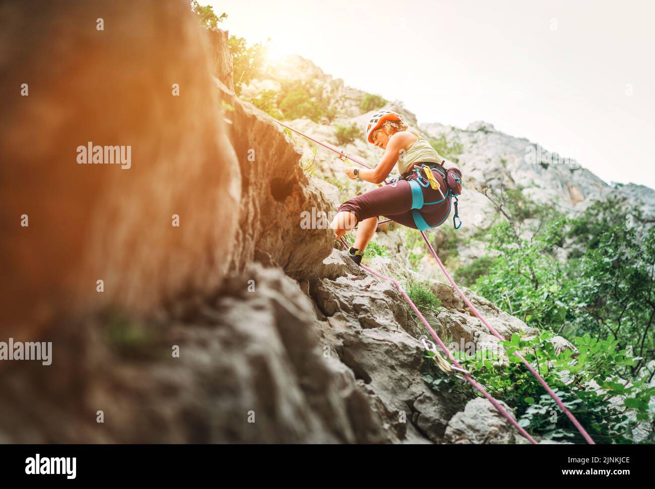 Active climber woman in protective helmet abseiling from cliff rock
