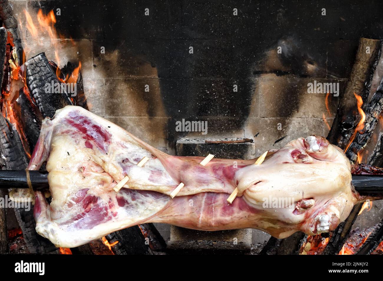 The carcass of a young sheep roasting on a spit over a low fire in oven. Roasted lamb on a spit. Kitchen in the open air. Local cuisine in Dagestan. R Stock Photo