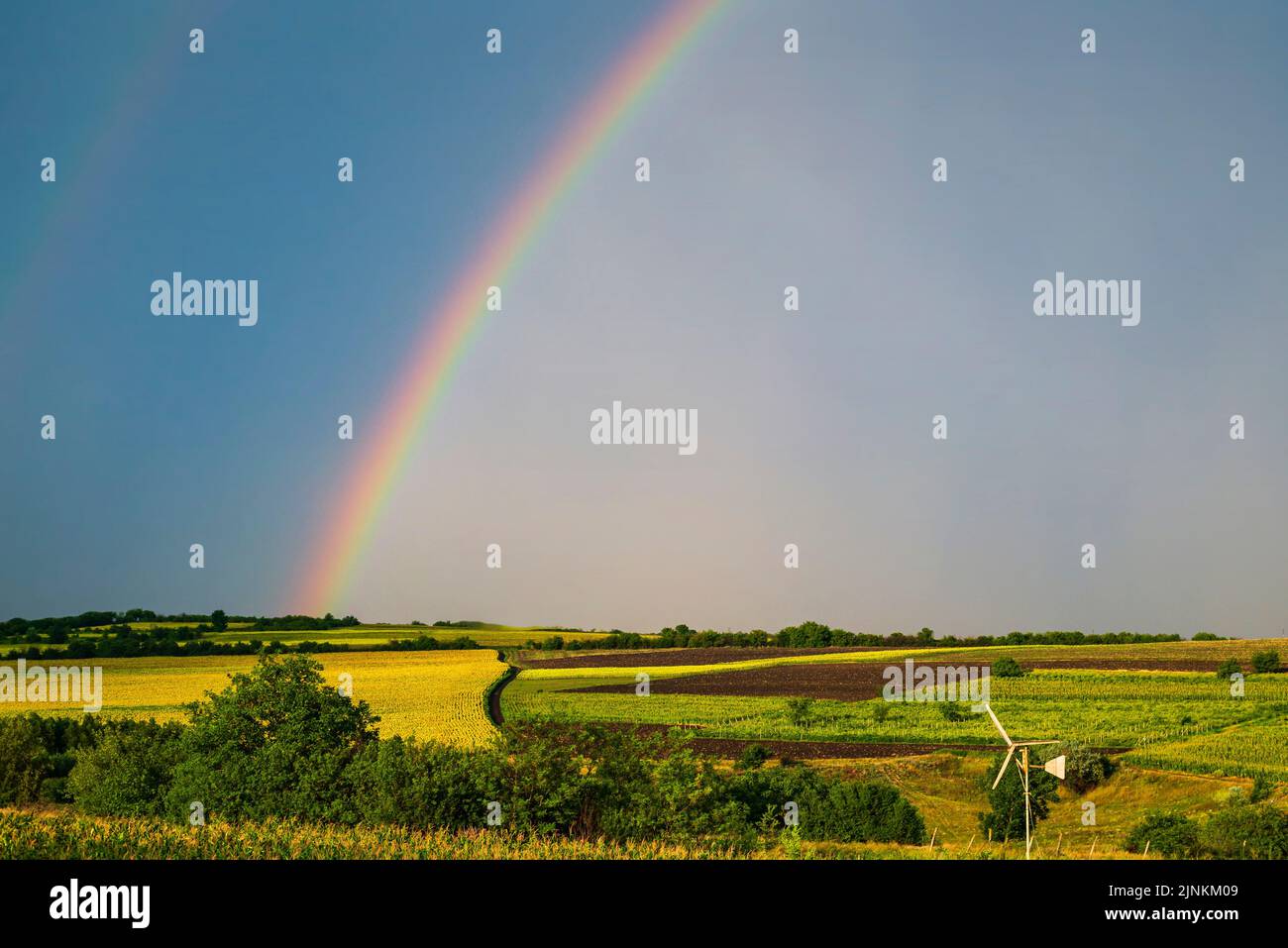 Rainbow over stormy sky. Rural landscape with rainbow over dark stormy sky in a countryside at summer day. Stock Photo