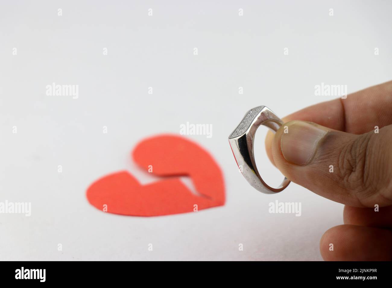 Relationship or love Proposal with a ring but that leads to heartbreak concept shown with a red paper broken heart and a silver ring Stock Photo