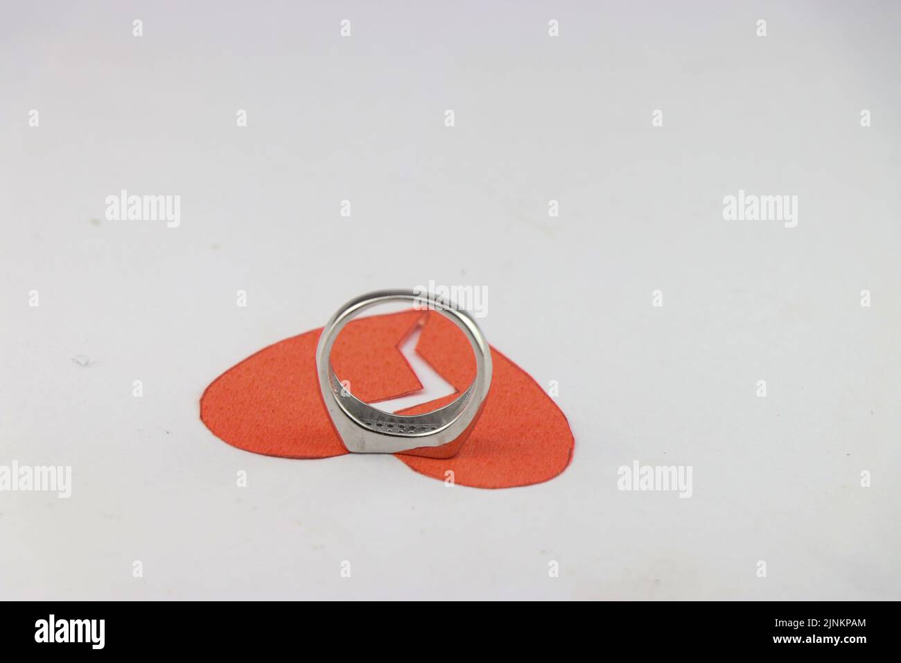 The red paper heart that is broken but the ring is trying to hold it together shows the concept of saving a relationship Stock Photo