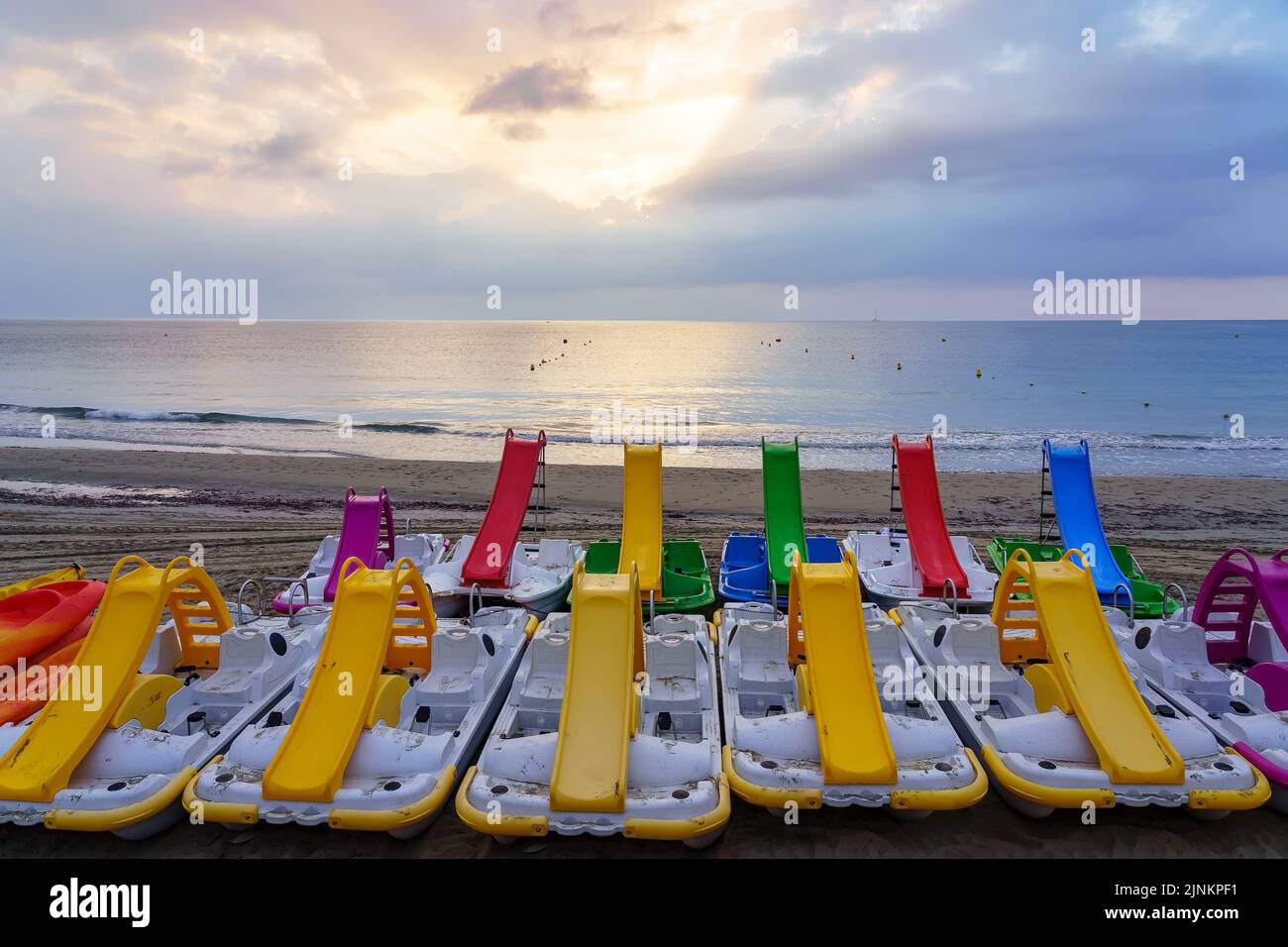 Pedal boats with a slide of many colors on the beach at sunrise Stock