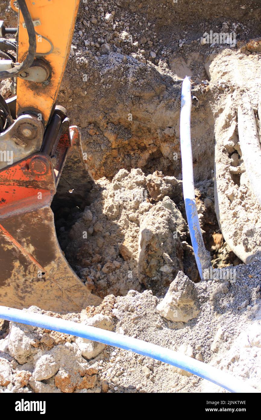 The grab of an excavator digs into the ground next to a cable Stock Photo