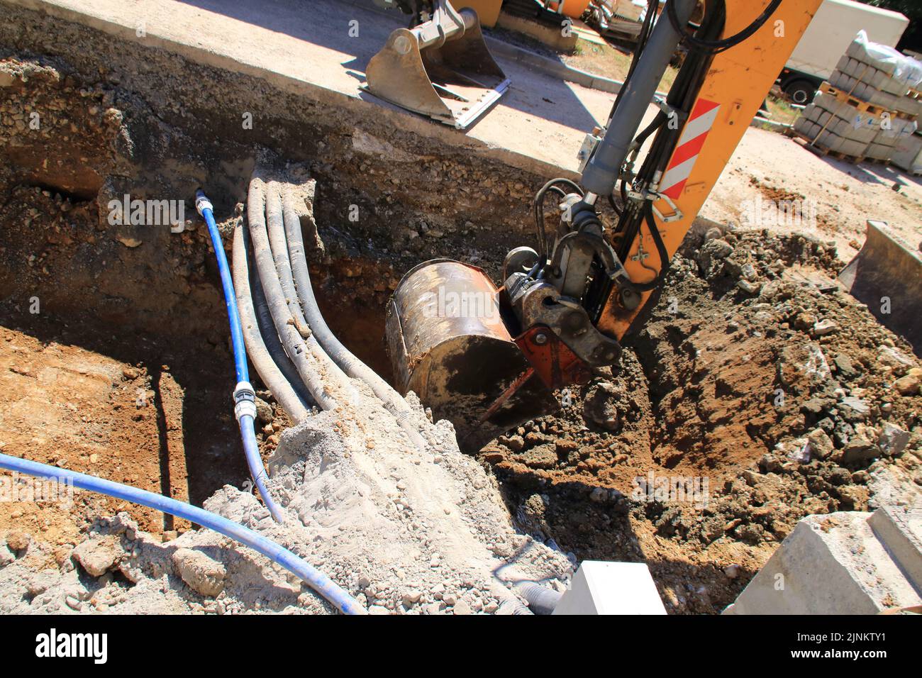 The grab of an excavator digs into the ground next to a cable Stock Photo