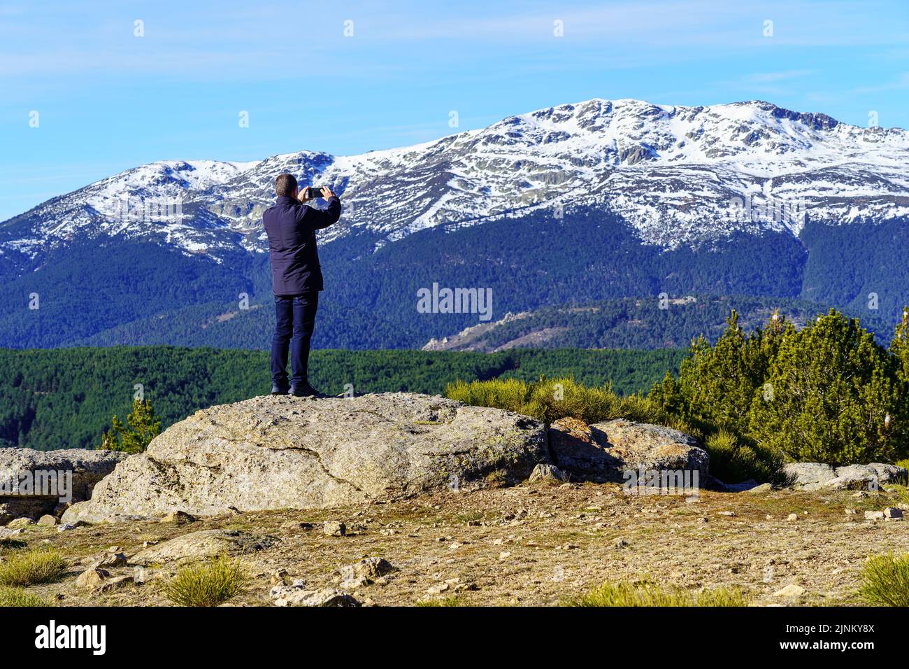 Man climbed on a rock and taking photos with his mobile to the mountains. Morcuera Madrid. Stock Photo