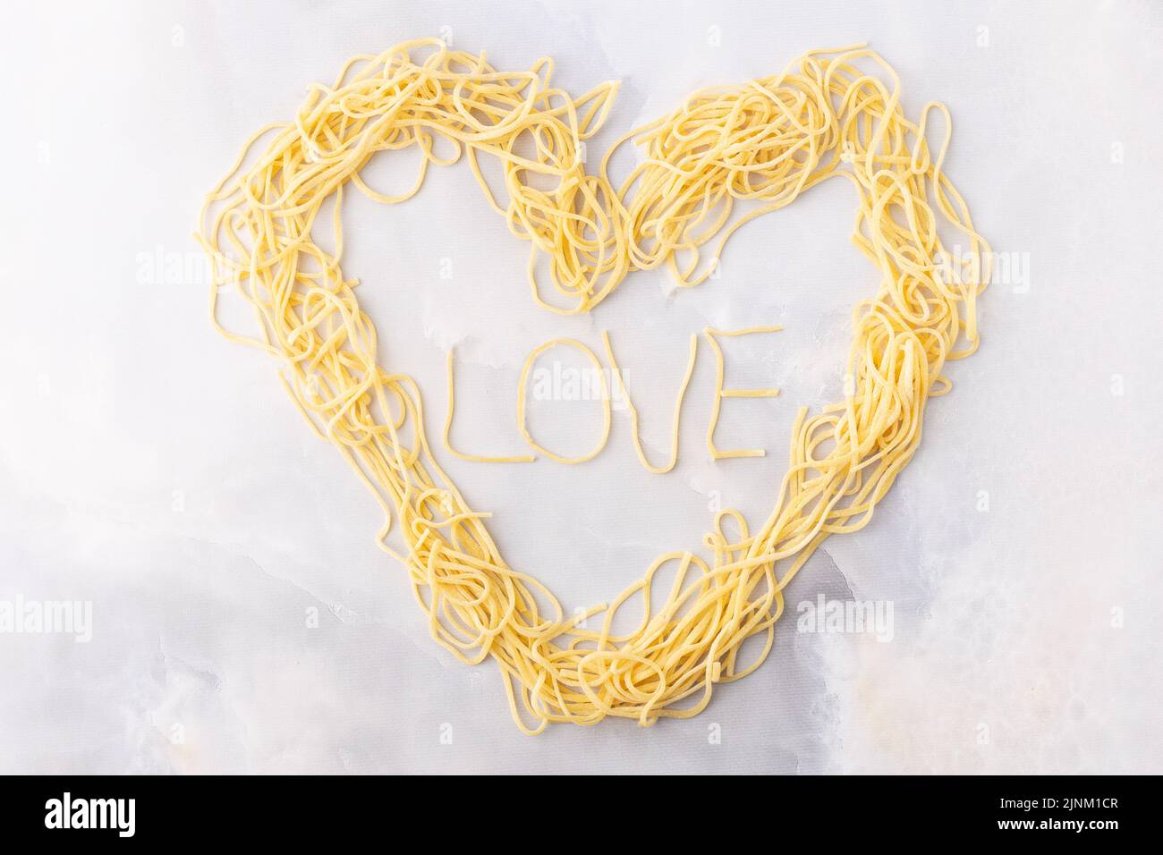 Decorative heart shaped pasta still life formed of pasta topped with tomatoes, basil Stock Photo