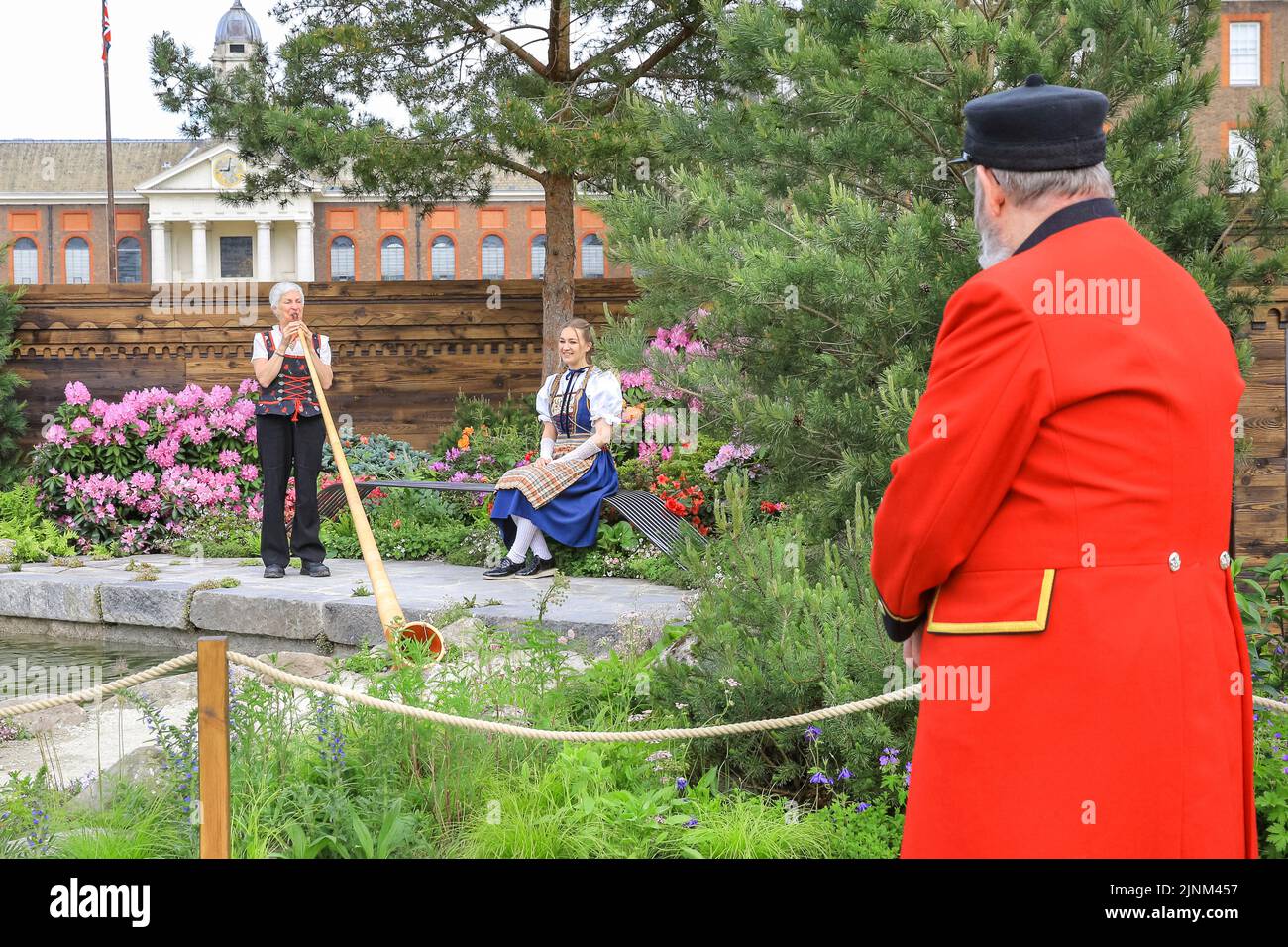 A Chelsea Pensioner watches and alphorn player in the 'Swiss Sanctuary Garden' by Lilly Gomm, Chelsea Flower Show 2022 Stock Photo