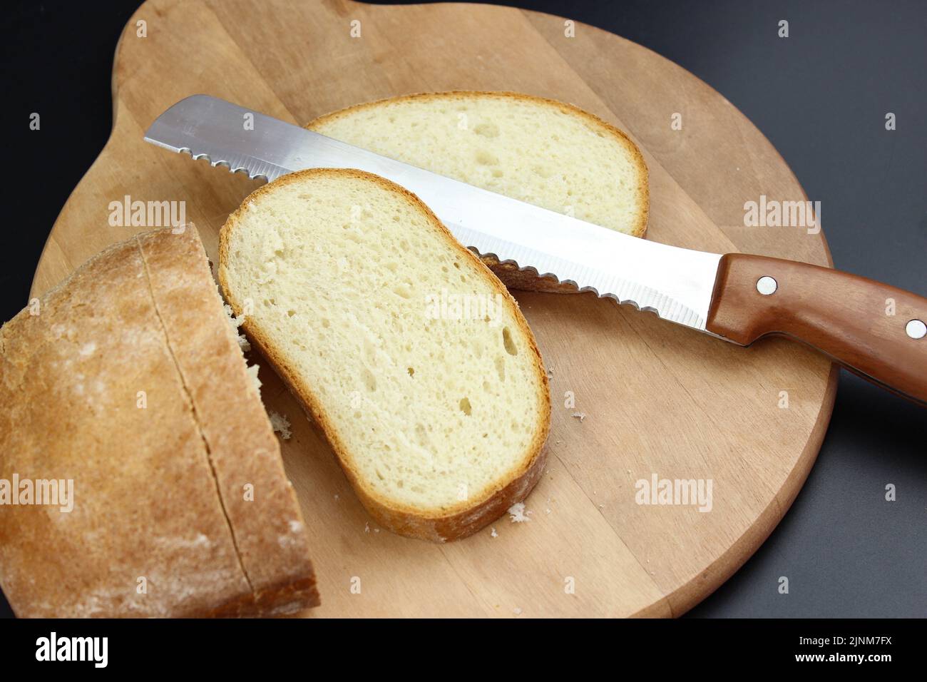 A large knife cuts thin pieces of white bread from a rectangular loaf Stock Photo