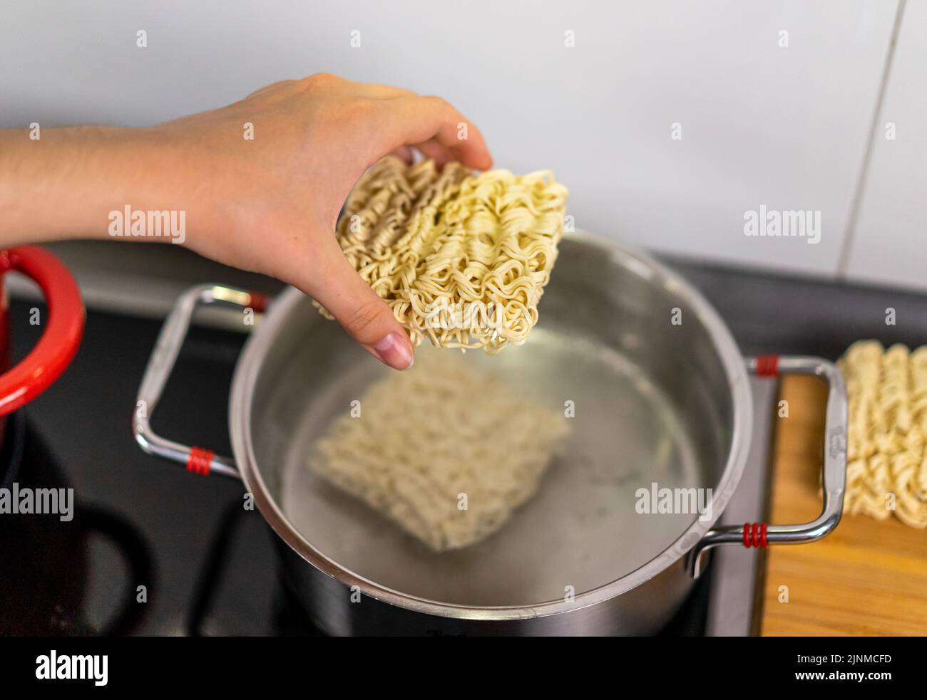 Young woman holds a piece of raw pasta ready to be thrown into boiling hot water Stock Photo