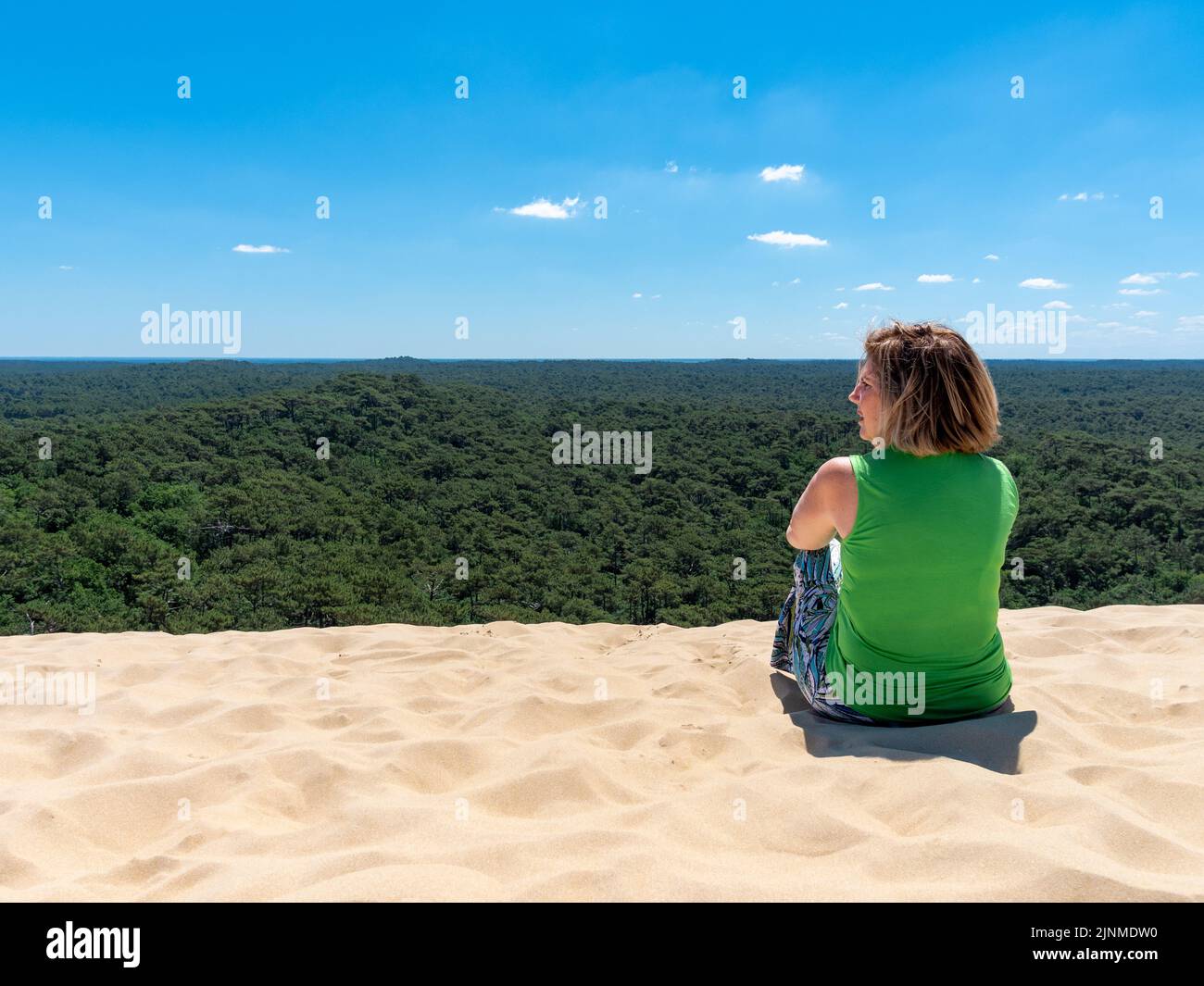 Mature caucasian woman setting on top of Dune of Pilat in Arcachon France Stock Photo