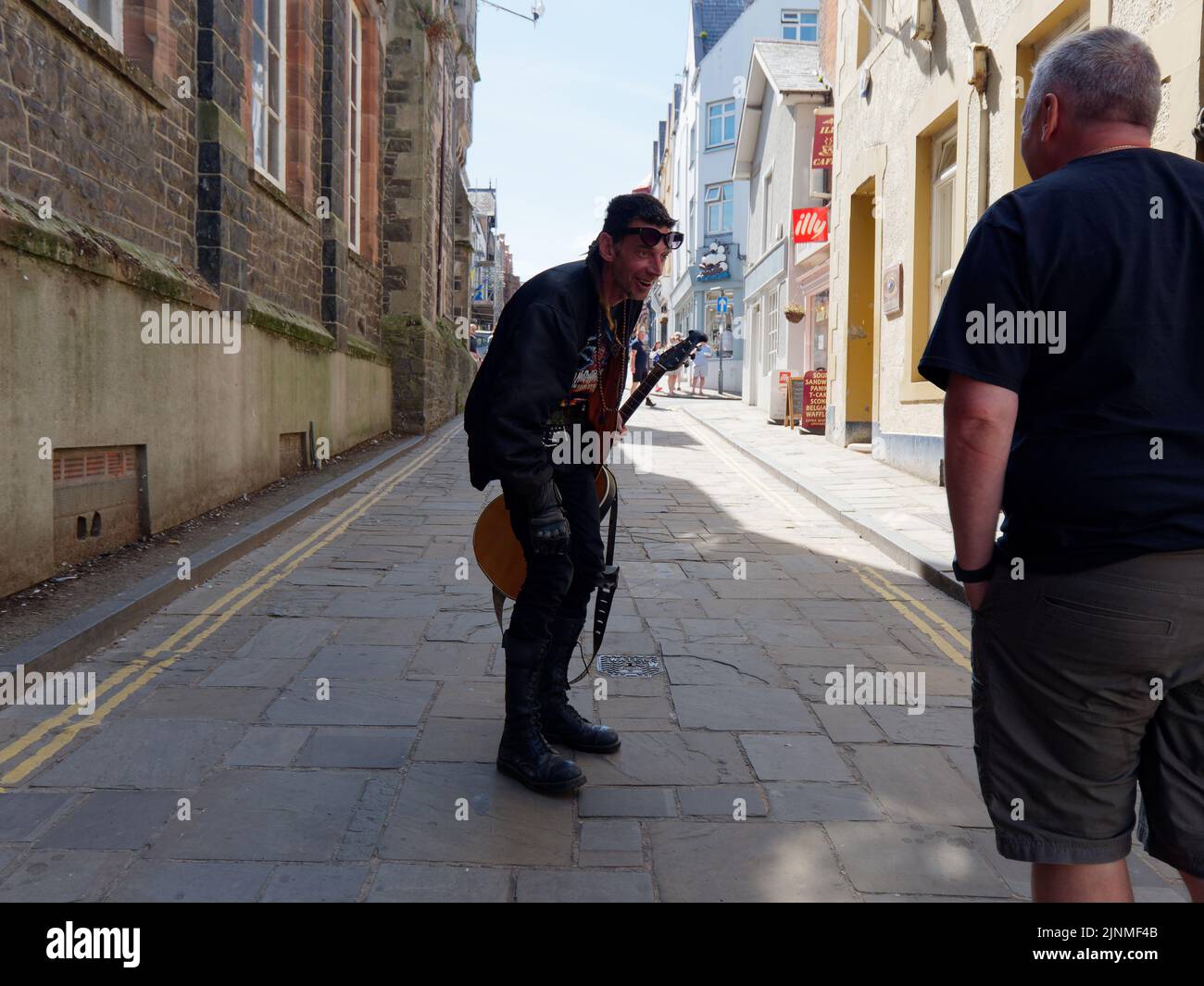 Conwy, Clwyd, Wales, August 07 2022: Busker with guitar looking at someones t shirt with a surprised look on his face. Stock Photo