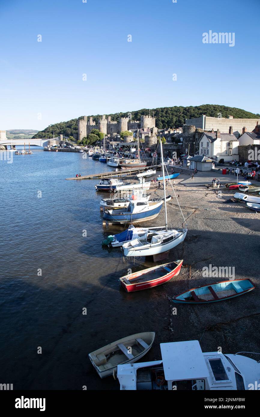 Holiday makers and tourists enjoying the evening sunshine at Conwy Harbour and beach, North Wales with the imposing Conwy castle in the background Stock Photo