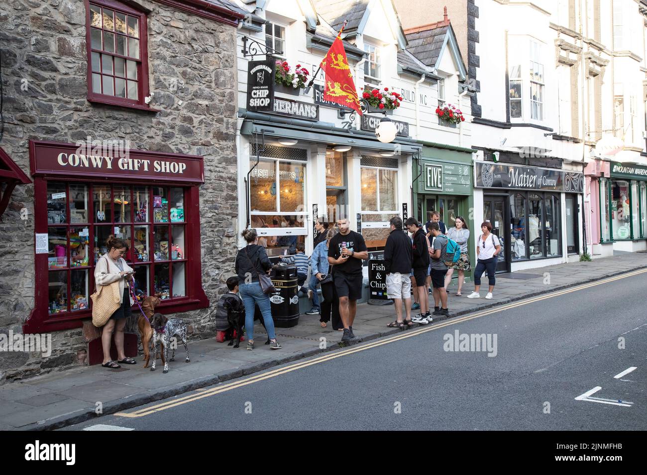Holiday makers and tourists queuing at the local Fish and Chip shop in Castle Street, Conwy, North Wales in mid summer Stock Photo