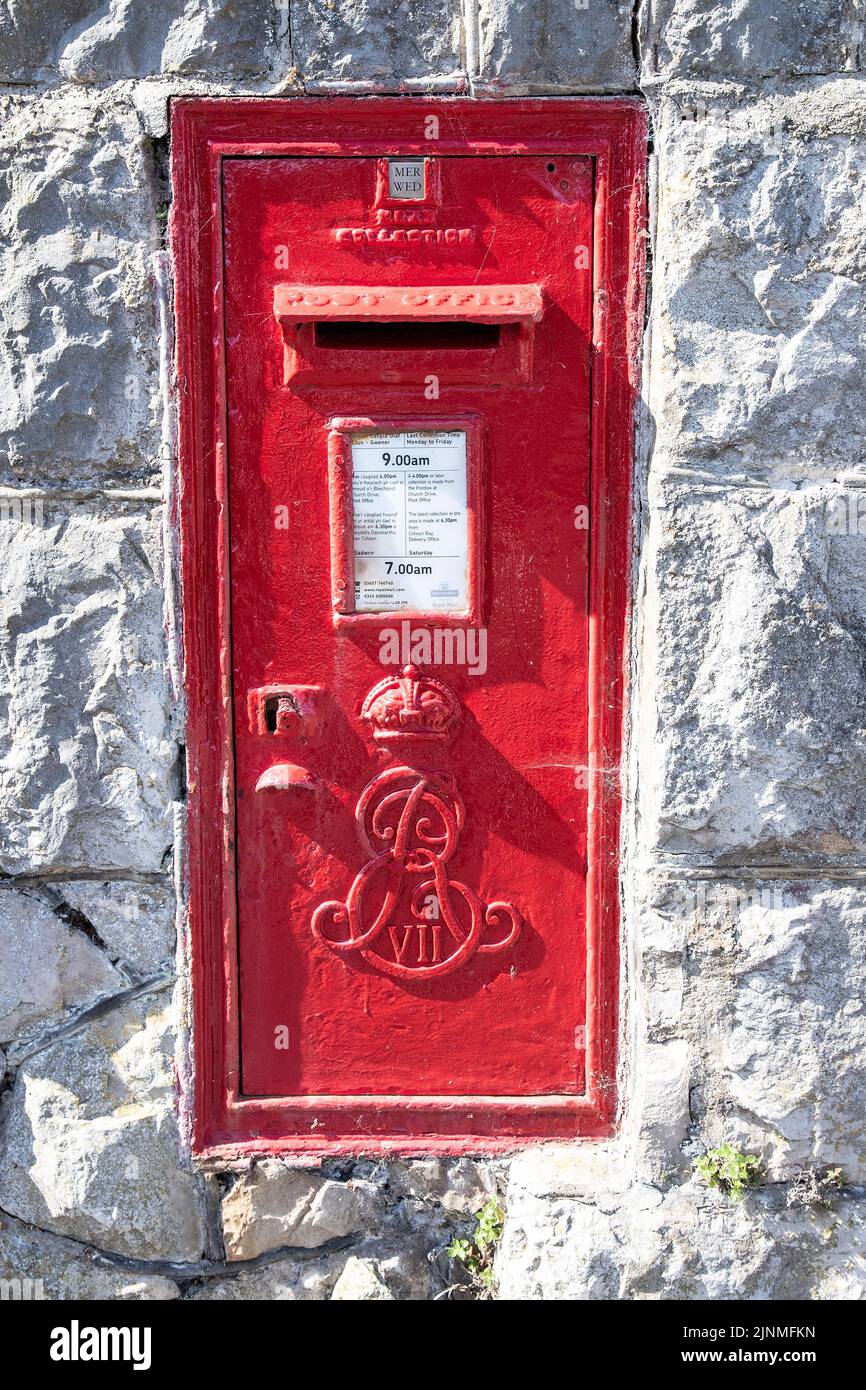 A post-box mounted in a stone wall with bilingual information in English & Welsh situated in Rhos On Sea North Wales, U.K. Stock Photo