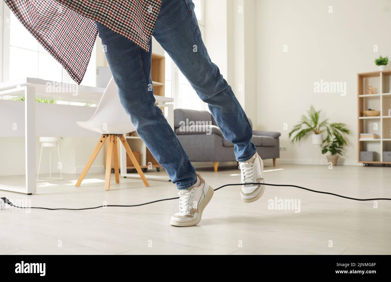Man falls down as he stumbles over a power cable on the floor in the living room Stock Photo