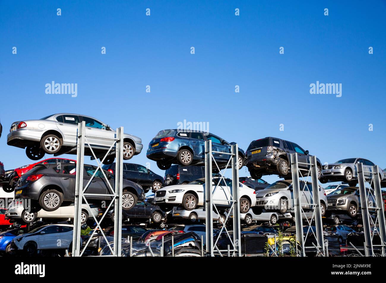 Profile view of scrap motor cars involved in road traffic accidents stacked up on racks in a scrap metal dealers junk yard with copy space Stock Photo