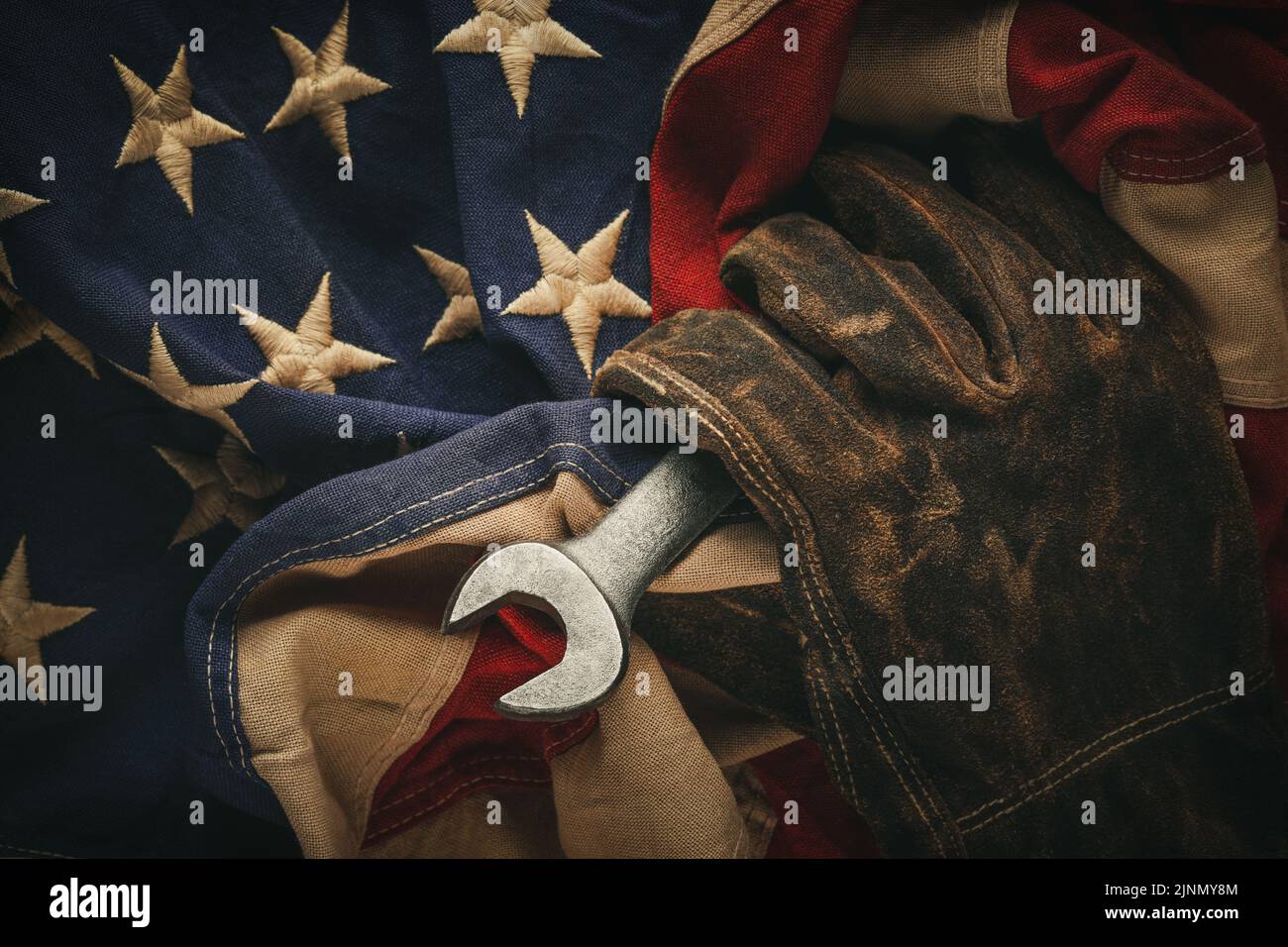 Worn work glove holding old wrench and US American flag. Made in USA, American workforce, blue collar worker, or Labor Day concept. Stock Photo