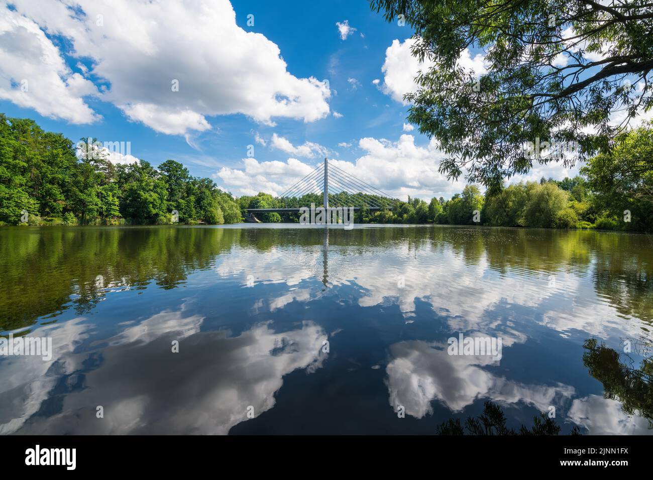 Shiny rippled water surface with sky reflection. Idyllic summer landscape with road cable-stayed bridge over Jordan pond in South Bohemian Tabor city. Stock Photo