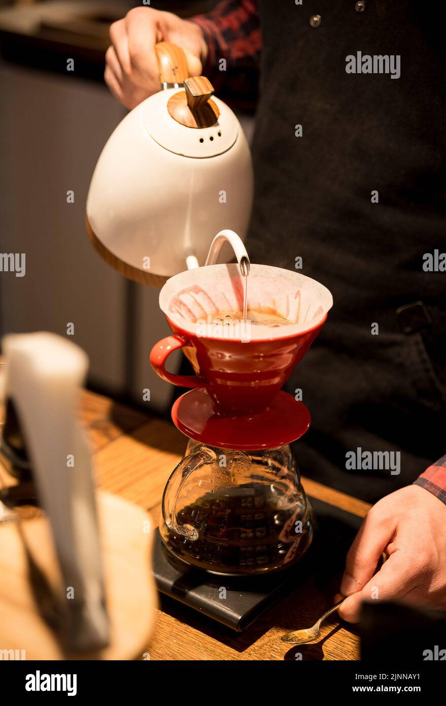 the barista spills hot water and makes coffee using the funnel method. the barista works behind the counter. Stock Photo