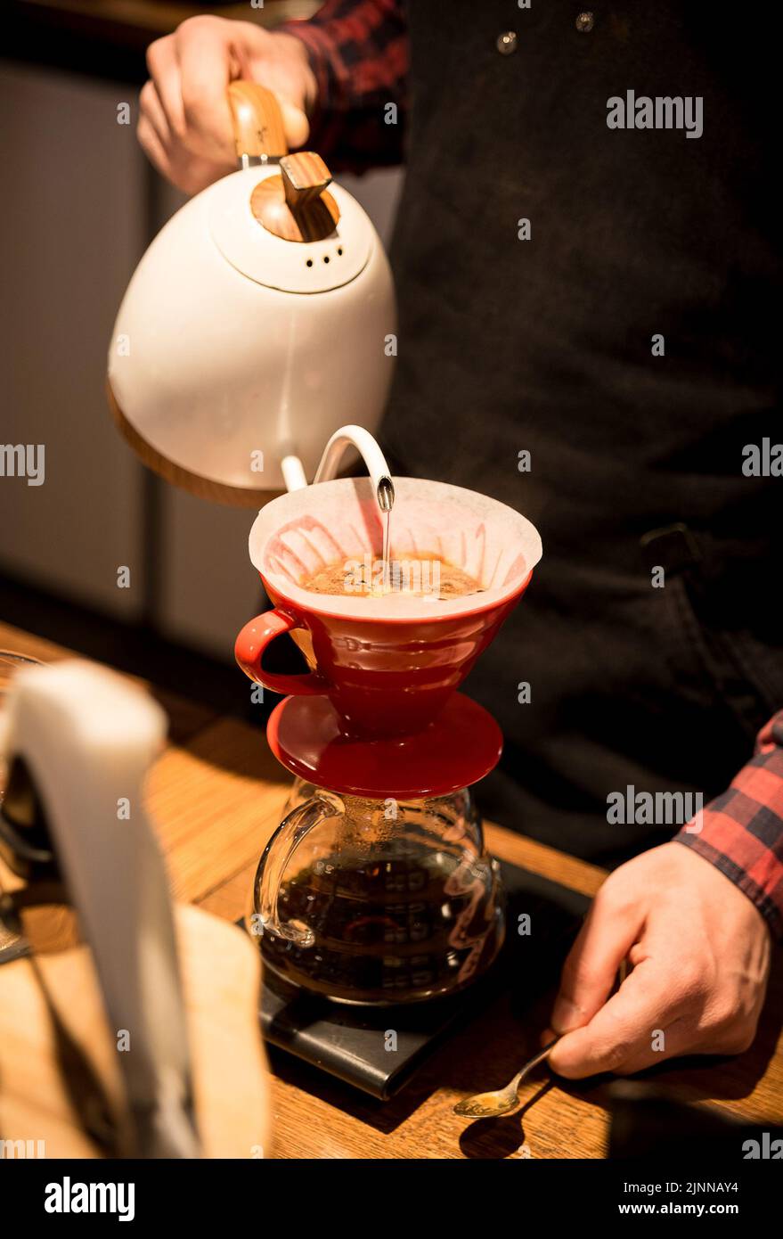 the barista spills hot water and makes coffee using the funnel method. the barista works behind the counter. Stock Photo