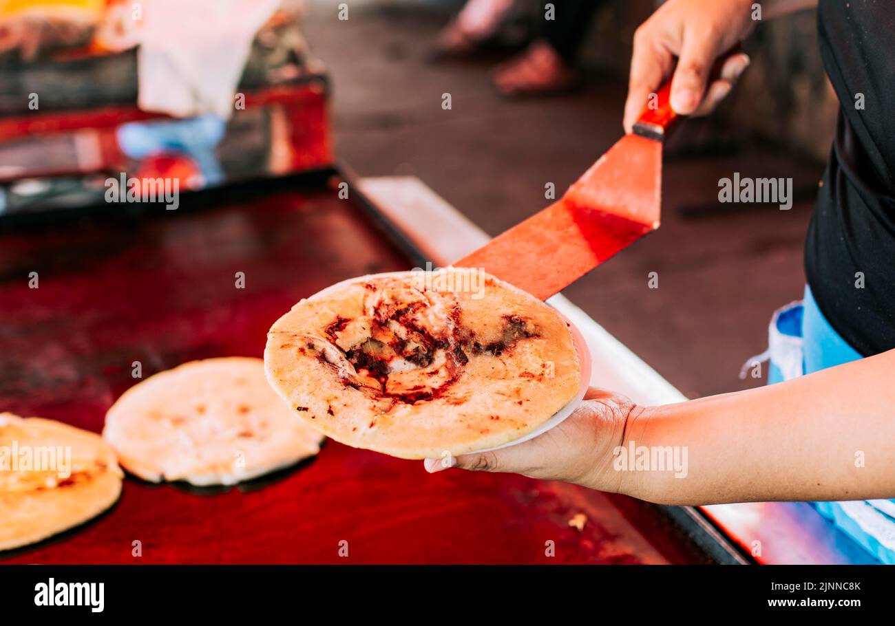 Hand holding a freshly made pupusa on a plate, Close up of traditional pupusa served on a plate. Traditional Salvadoran pupusas freshly made with Stock Photo