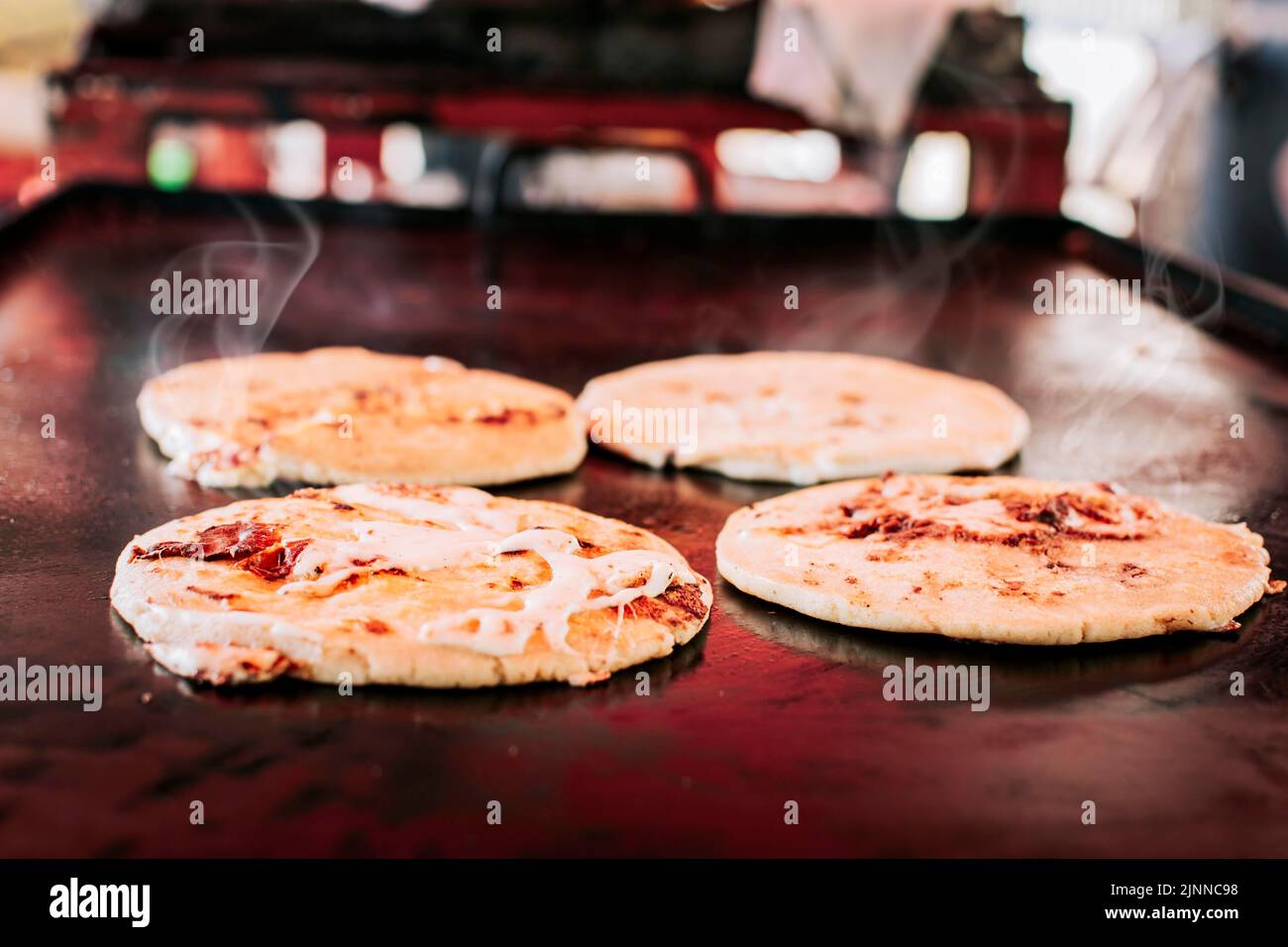 Traditional Salvadoran pupusas with melted cheese on a grill, Traditional cheese pupusas on the grill. Side view of four traditional crispy pupusas Stock Photo