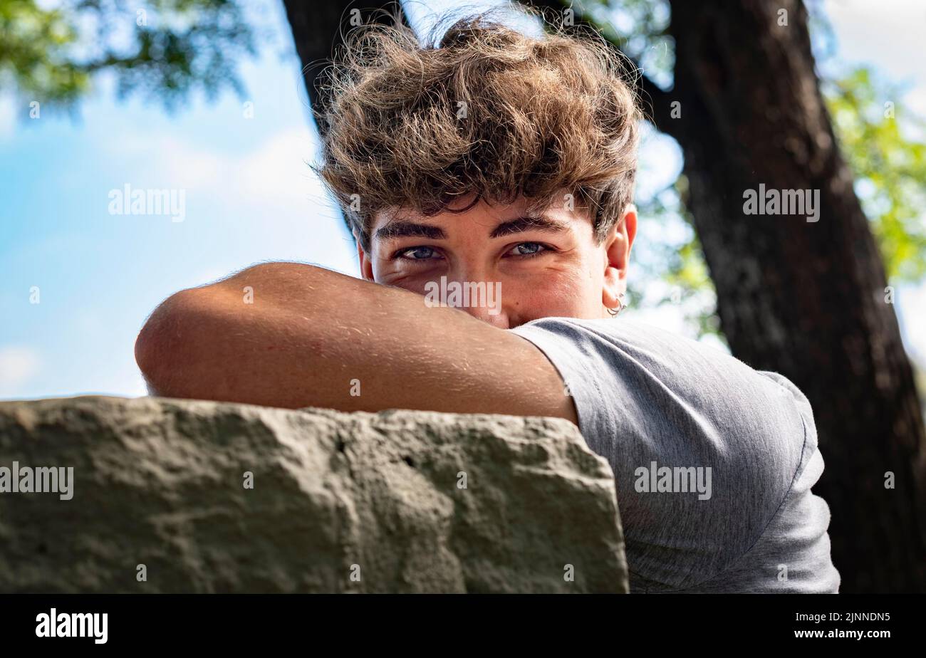 Young man falls his head down on his arms in a public park. He is looking at camera Stock Photo