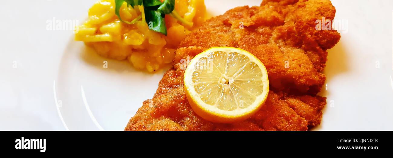 Delicious golden-brown fried Wiener Schnitzel with potato salad and a slice of lemon on a white plate Stock Photo