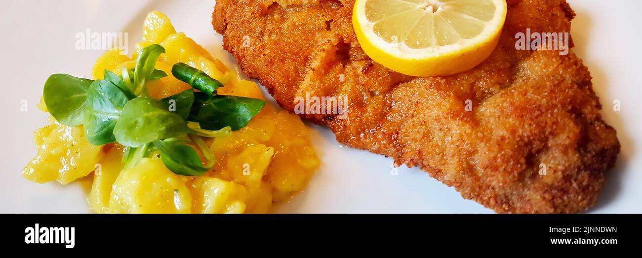Delicious golden-brown fried Wiener Schnitzel with potato salad and a slice of lemon on a white plate Stock Photo