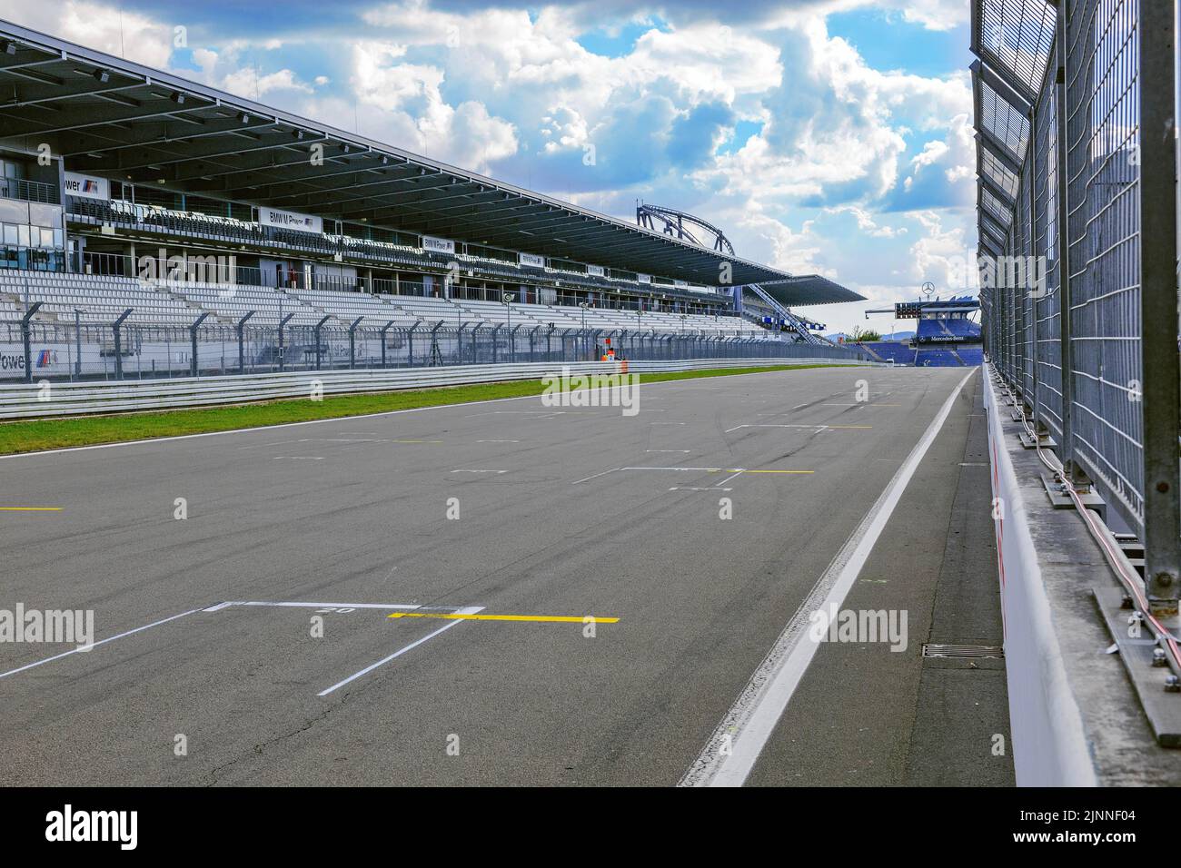 View through security fence from pit lane to empty start-finish straight grid lane with markings for start position, main grandstand on left Stock Photo