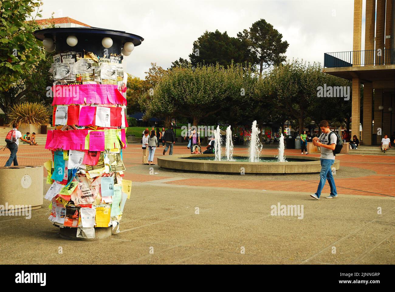 A male student walks through Sproul plaza, passing a kiosk adorned with fliers, as he enters the campus of the University of California Berkeley Stock Photo