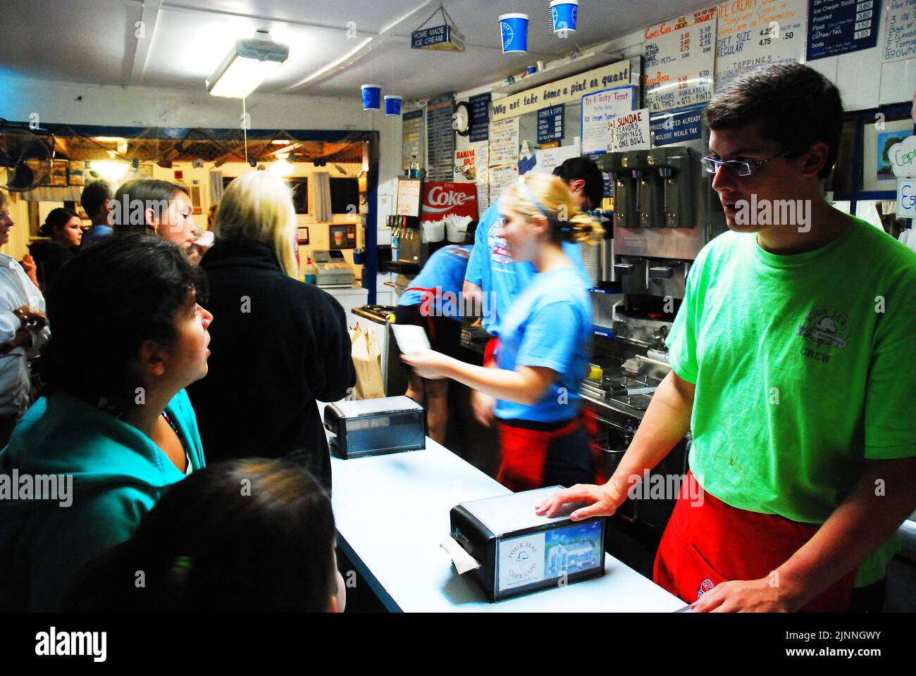 A teenager worker, on a summer job at a busy ice cream parlor, takes an