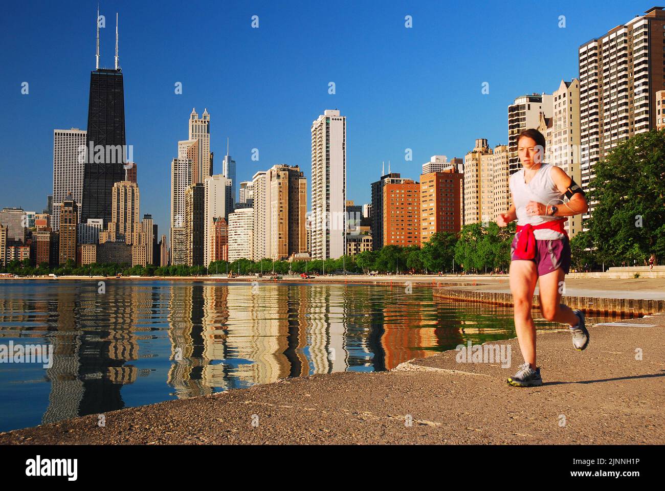 A young woman jogger keeps a healthy lifestyle while running along the shore of Lake Michigan within sight of the Chicago skyline Stock Photo