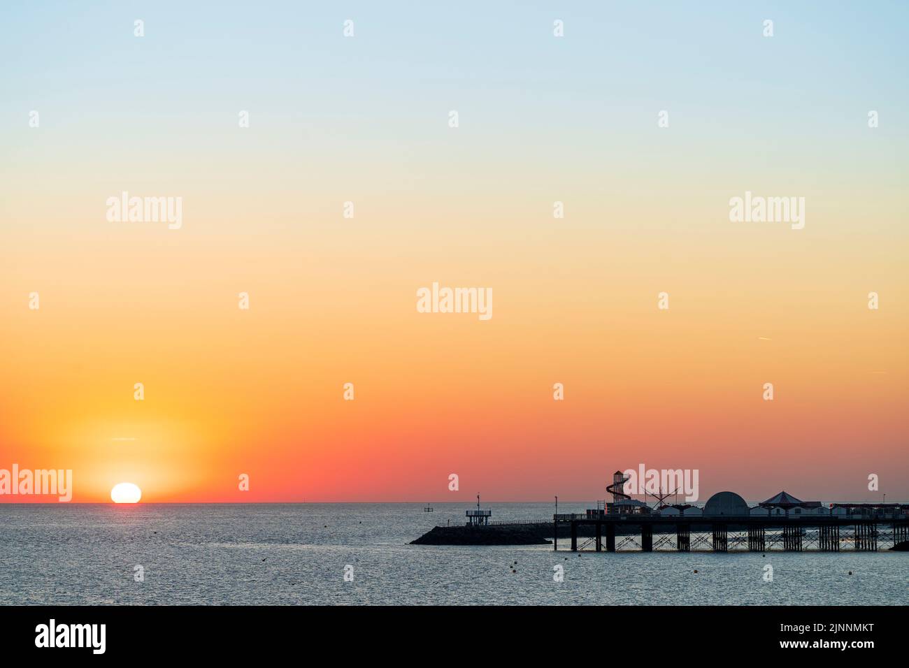 Sunrise over the North sea at Herne Bay in Kent. Sun rising above the sea with the silhouette of the Herne Bay pier and harbour jetty. Sky is orange turning gradually into blue. Stock Photo