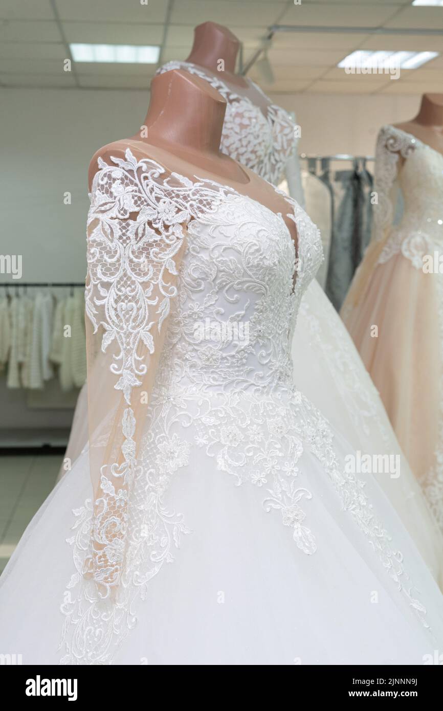 A beautiful white wedding dress on a mannequin. A close-up of a dress against other wedding dresses in a bridal shop. Stock Photo