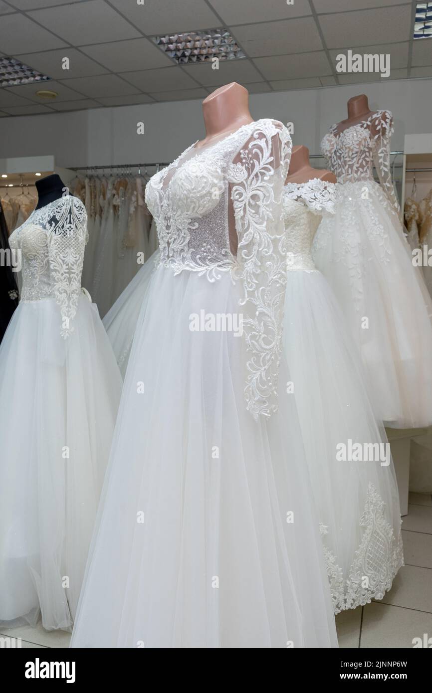 A beautiful white wedding dress on a mannequin. A close-up of a dress against other wedding dresses in a bridal shop Stock Photo