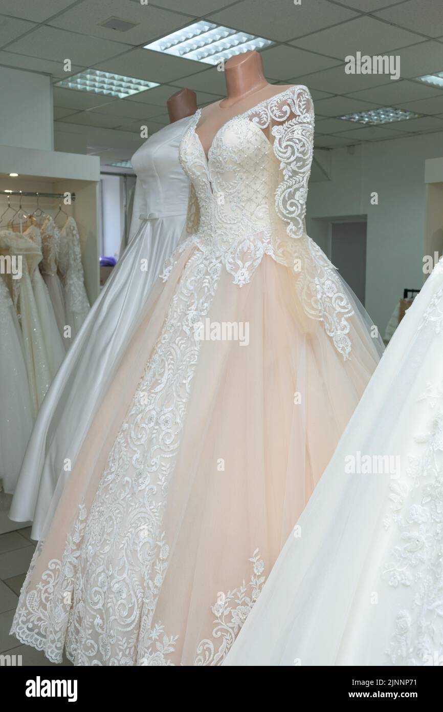 A beautiful cream wedding dress on a mannequin. A wedding dress on the background of other wedding dresses in a wedding salon Stock Photo