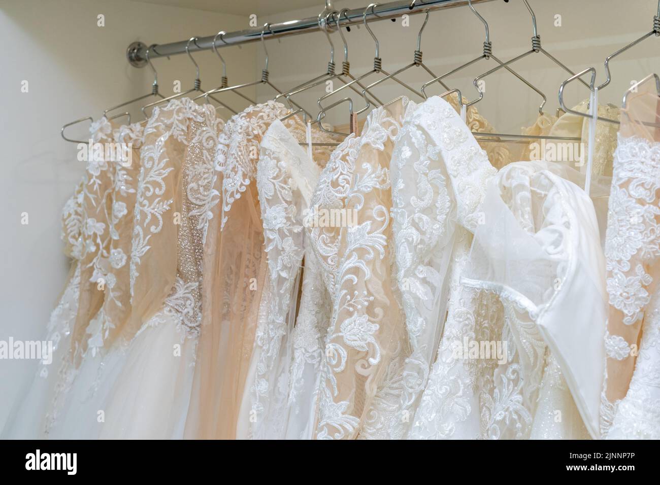 White and cream wedding dresses on a hanger in a bridal boutique. Close up Stock Photo