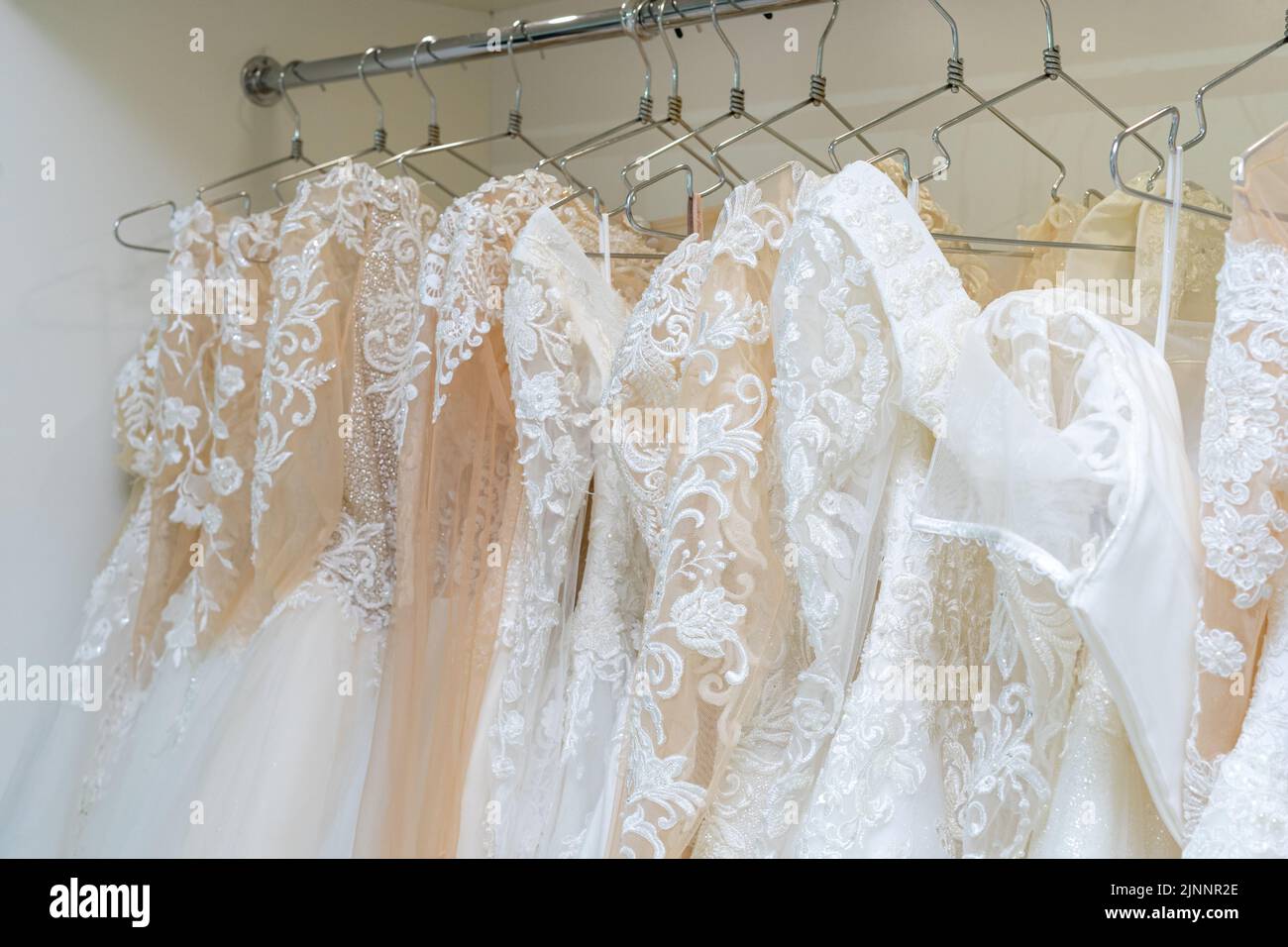 White and cream wedding dresses on a hanger in a bridal boutique. Close up Stock Photo